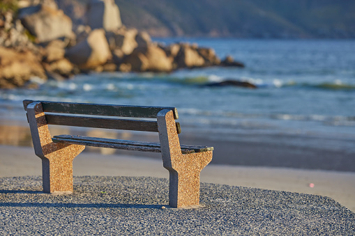 Empty wooden rest bench at sea shore by sunny summer day