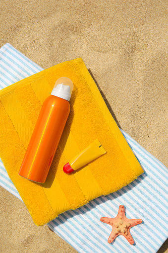 Sunscreen, lip balm, starfish and towels on sand, top view. Sun protection care