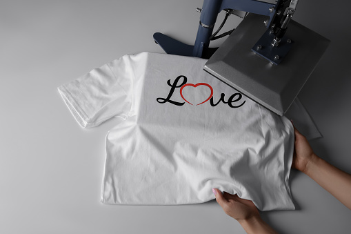 Printing logo. Woman with t-shirt using heat press at white table, above view