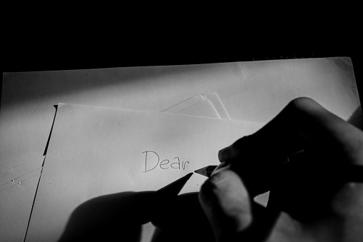 write the word dear on paper, write a love letter for a lover, writing in a room with minimal light, the shadow of the hand of the person writing