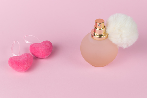 A bottle of women's perfume and two red hearts on a pink background. Women's perfumes.