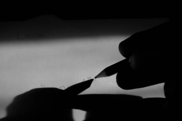 hand writing with a pencil on paper, writing in a room with minimal light, writing activity