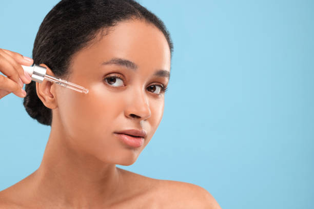 istock Beautiful woman applying serum onto her face on light blue background. Space for text 1921007421