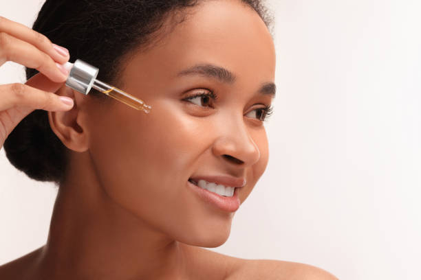 istock Smiling woman applying serum onto her face on white background, closeup 1921013699