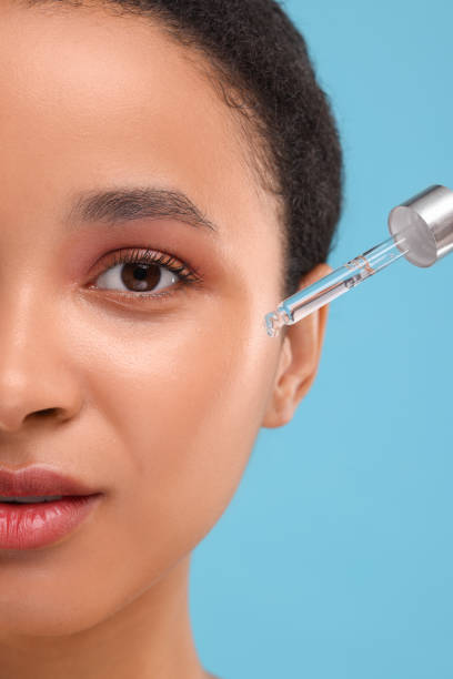istock Woman applying serum onto her face on light blue background, closeup 1921013703
