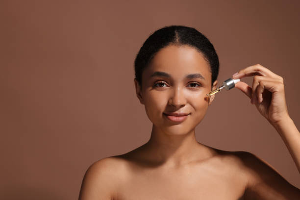 istock Beautiful woman applying serum onto her face on brown background. Space for text 1921014751