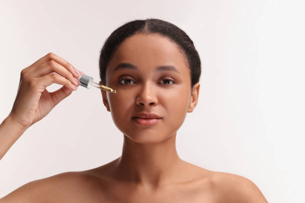 istock Beautiful woman applying serum onto her face on white background 1921019971