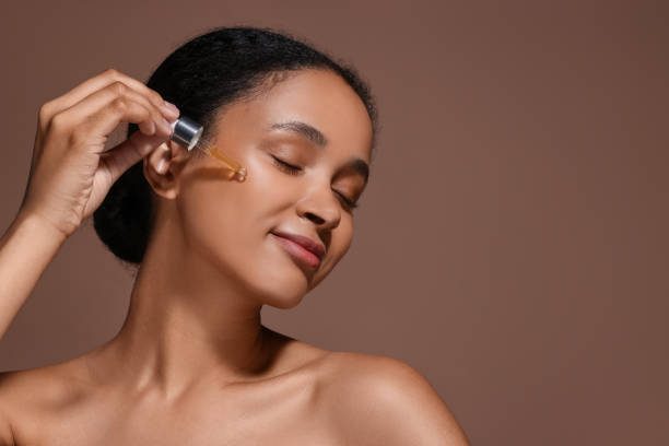istock Beautiful woman applying serum onto her face on brown background. Space for text 1921020493