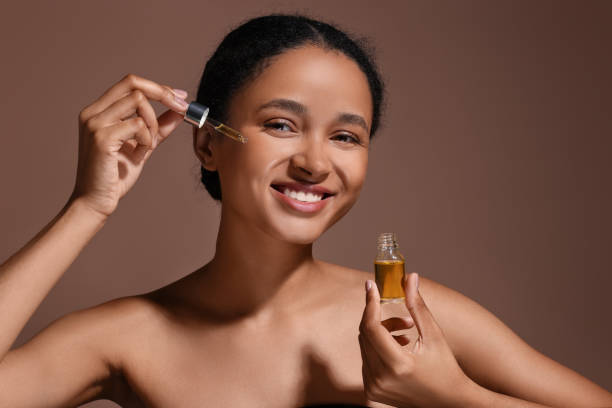 istock Smiling woman applying serum onto her face on brown background 1921020496