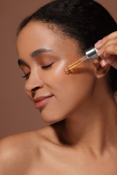 istock Beautiful woman applying serum onto her face on brown background 1921020497