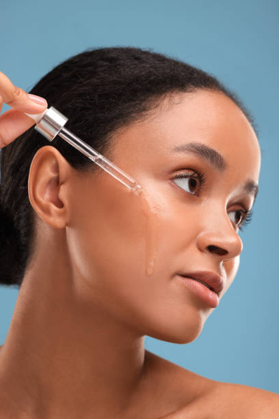 istock Beautiful woman applying serum onto her face on blue background 1921020773