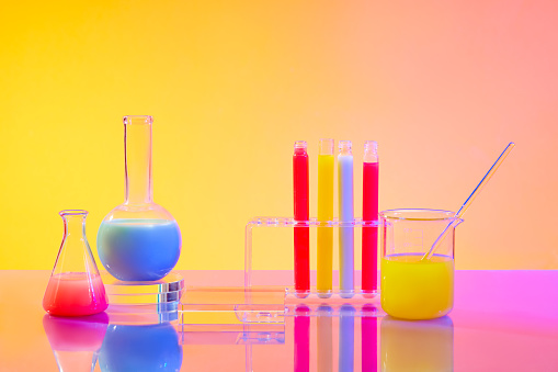 Close up of colorful liquids in test tubes and glass laboratory flasks on a pink yellow gradient background. Empty podium for product display with laboratory space.