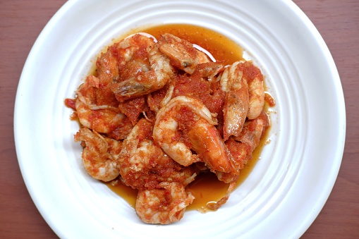 Schezwan Prawns in white plate with wooden background. Schezwan Prawns is indo-chinese cuisine curry dish with prawns or shrimps roasted in Schezwan Sauce. Udang saos Padang