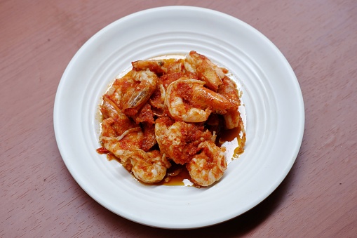 Schezwan Prawns in white plate with wooden background. Schezwan Prawns is indo-chinese cuisine curry dish with prawns or shrimps roasted in Schezwan Sauce. Udang saos Padang