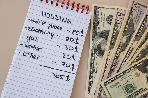 Dollar cash money with notebook handwritten housing expenses. Counting bills for electricity, gas, water. Concept of Efficient Consumption and Economy. Spending habits