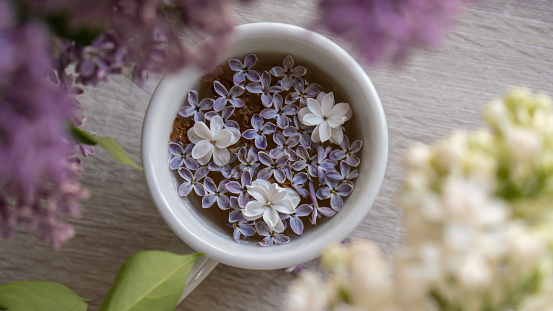 Tasty black tea in white cup on windowsill with aromatic lilac flowers. Spring composition Cup of lilac tea drinking recipe flowering branches of purple lilac. Still life for copy space greeting card, poster, banner, wallpaper. Relaxation and natural ingredients