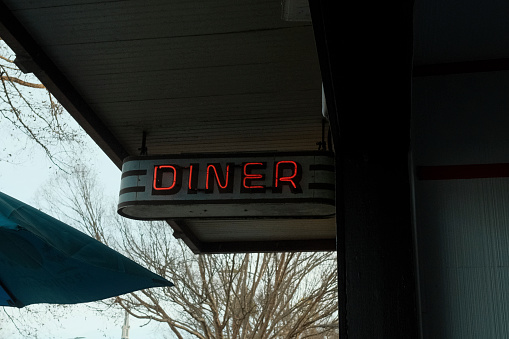 Red neon diner sign in a small town cityscape.