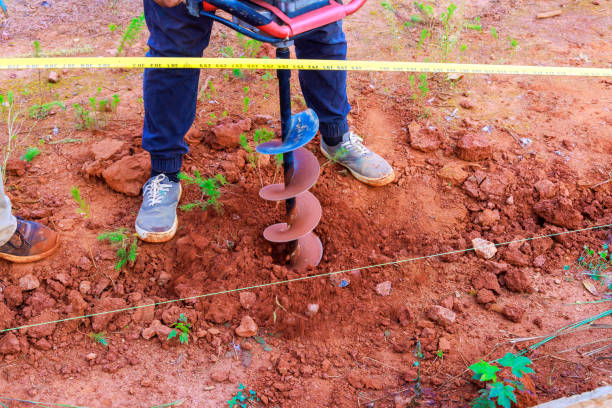 Worker digs ground with a gasoline drilling machine in for fence posts