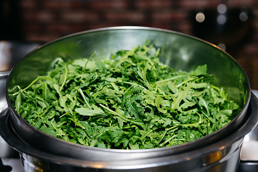 A metal bowl overflowing with fresh, green arugula leaves, ready for a healthy salad or garnish.