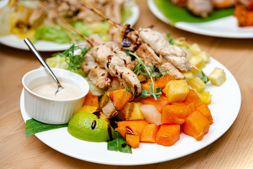 Succulent grilled chicken skewers paired with a sweet assortment of tropical fruit salad, complemented by a tangy lime wedge and creamy dipping sauce.