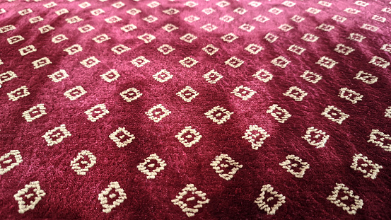 White ornamental motifs on a thick red rug or carpet photographed from a perspective angle