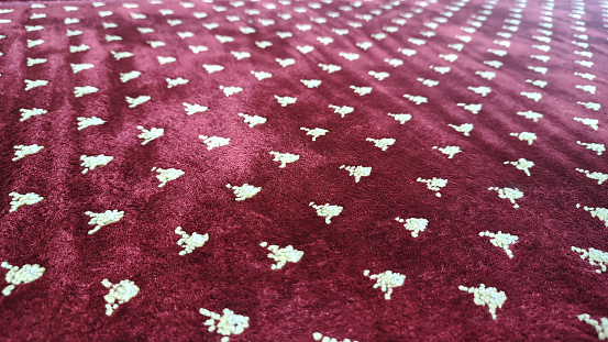 White ornamental motifs on a thick red rug or carpet photographed from a perspective angle