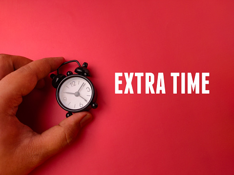 Hand holding alarm clock with the word EXTRA TIME on a red background