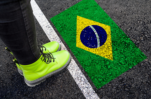 a womman with a boots standing on asphalt next to flag of Brazil and border
