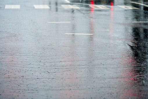 Sheets of water run downhill atop asphalt at a busy intersection during a torrential rain storm on a late winter afternoon.