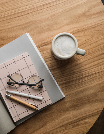 Morning - a mug of coffee with milk, a magazine, a diary, glasses on a wooden table, top view