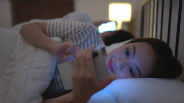 portrait of beautiful asian woman using mobile phone on bed at night - sleeping lying on back couple bed zdjęcia i obrazy z banku zdjęć