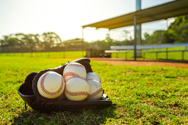 бейсбольная перчатка, наполненная бейсбольными мячами, сидит на поле для игры в мяч перед пустой землянкой во время заката - baseball diamond стоковые фото и изображения