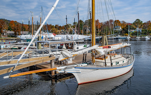 A boat with furled sails sits quietly by a wooden pier on an October day in Camden, Maine.