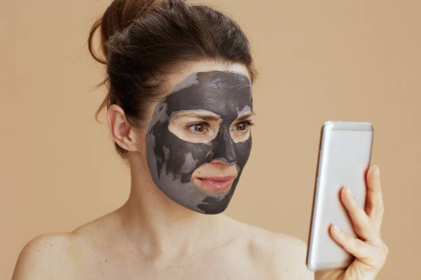 istock young woman with facial mask using smartphone 1921446920