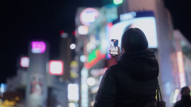 Woman using her mobile smart phone to take photos and videos in city Shibuya Tokyo at night
