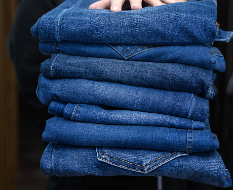 Hold a stack of blue pants, jeans pants in your hands close up isolated