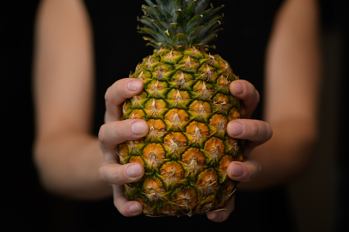 A man holds a ripe pineapple in his hand close up isolated