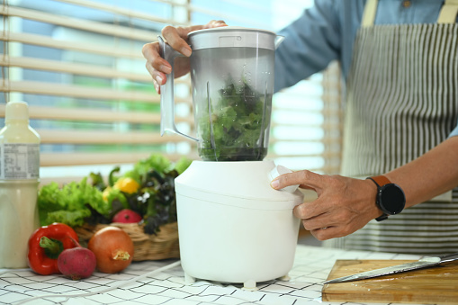 Senior man making vegetable smoothie with fresh vegetables in a blender. Healthy eating lifestyle concept.