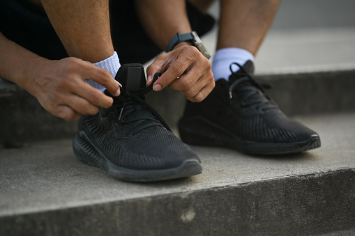 Cropped shot legs of sporty man tying shoelaces before jogging or cardio workout.