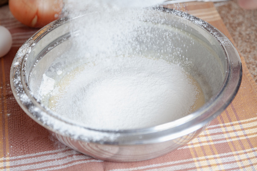 Sifted flour is poured into a metal bowl on a napkin