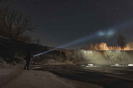 Man with a flashlight at Jagala waterfall in winter at night. High quality photo