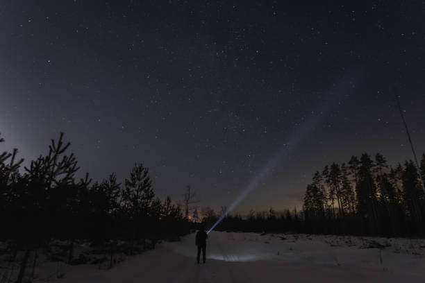 istock Night scene with starry sky, a man with a flashlight in the forest road in winter. 1921531749