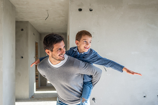 Young happy father and son looking their new apartment and having fun. It’s still construction.