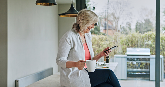 Woman, drinking coffee and smartphone or happy in kitchen, funny online conversation and social media. Smiling mature person, cellphone and internet connection or mobile app for communication at home