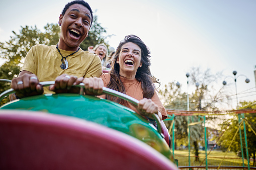 Young cheerful couple having fun on rollercoaster at amusement park. Copy space.