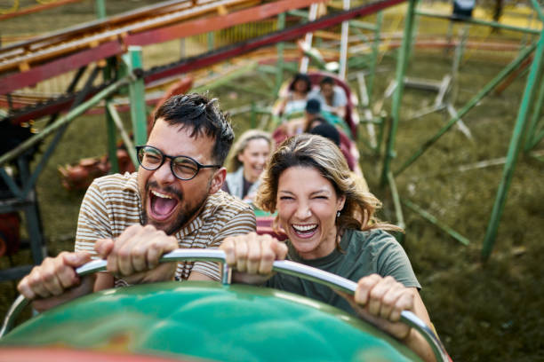 Cheerful couple riding on rollercoaster at amusement park. Young carefree couple having fun on rollercoaster ride at amusement park. rollercoaster stock pictures, royalty-free photos & images