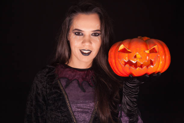 istock Lady in witch costume holding a pumpkin over black background 1921542249