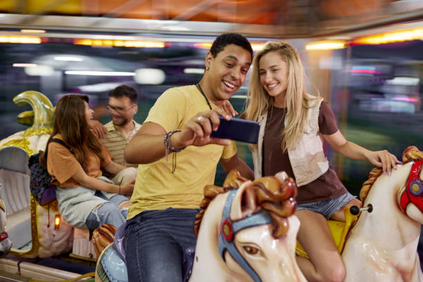Happy couple taking a selfie during carousel ride at amusement park.
