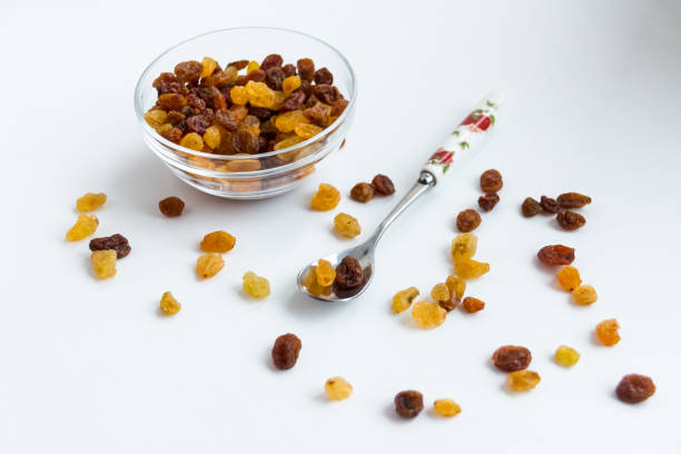multiple raisins isolated over the white background. Small dessert spoon with raisins. sultana. dry grapes.