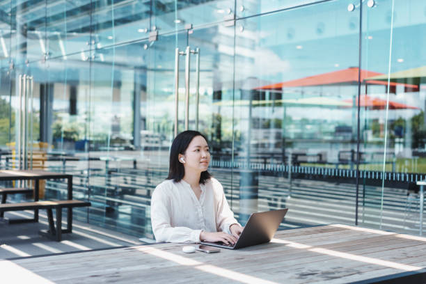 istock Young Asian woman working remotely on an outdoor table, using her laptop, bluetooth earphone and mobile phone 1921555890